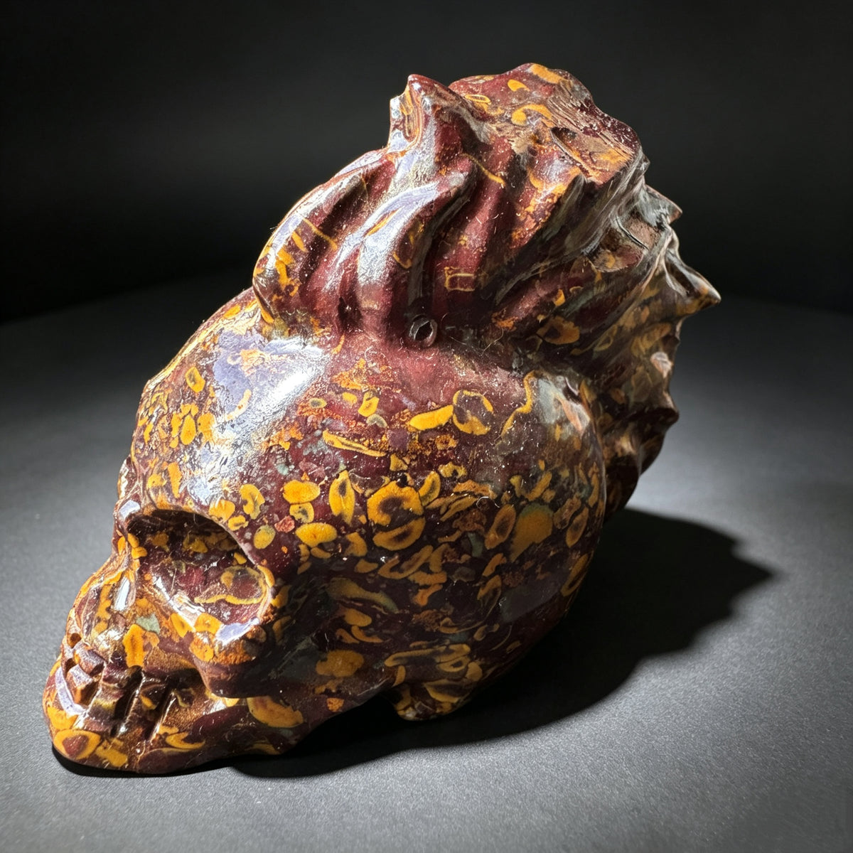 Natural stone carved skull sculpture with red, brown and golden natural patterns, shown from a right side angle.