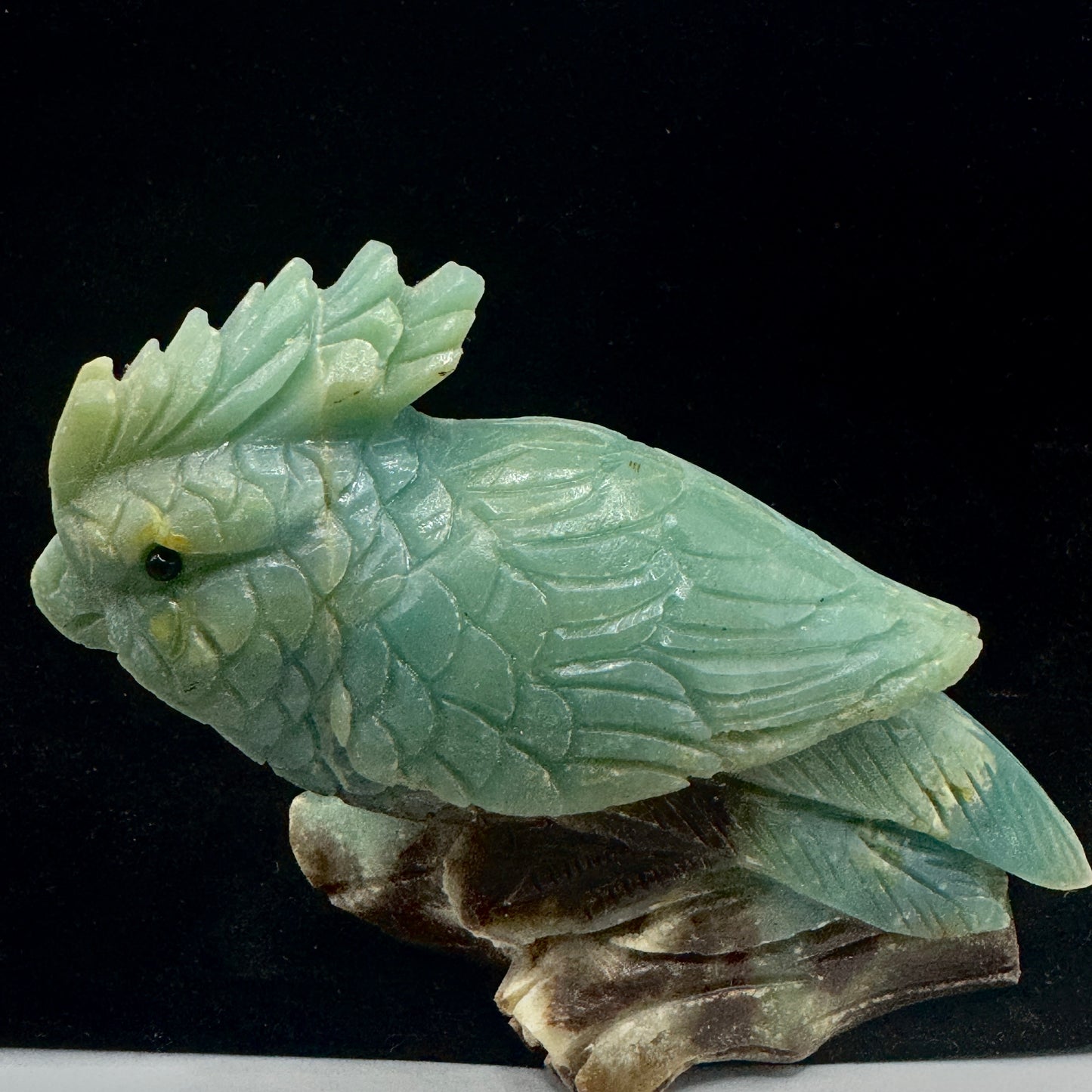 A side profile of the sculpture highlighting the intricate details of the parrot's curved wings and long, graceful tail feathers.