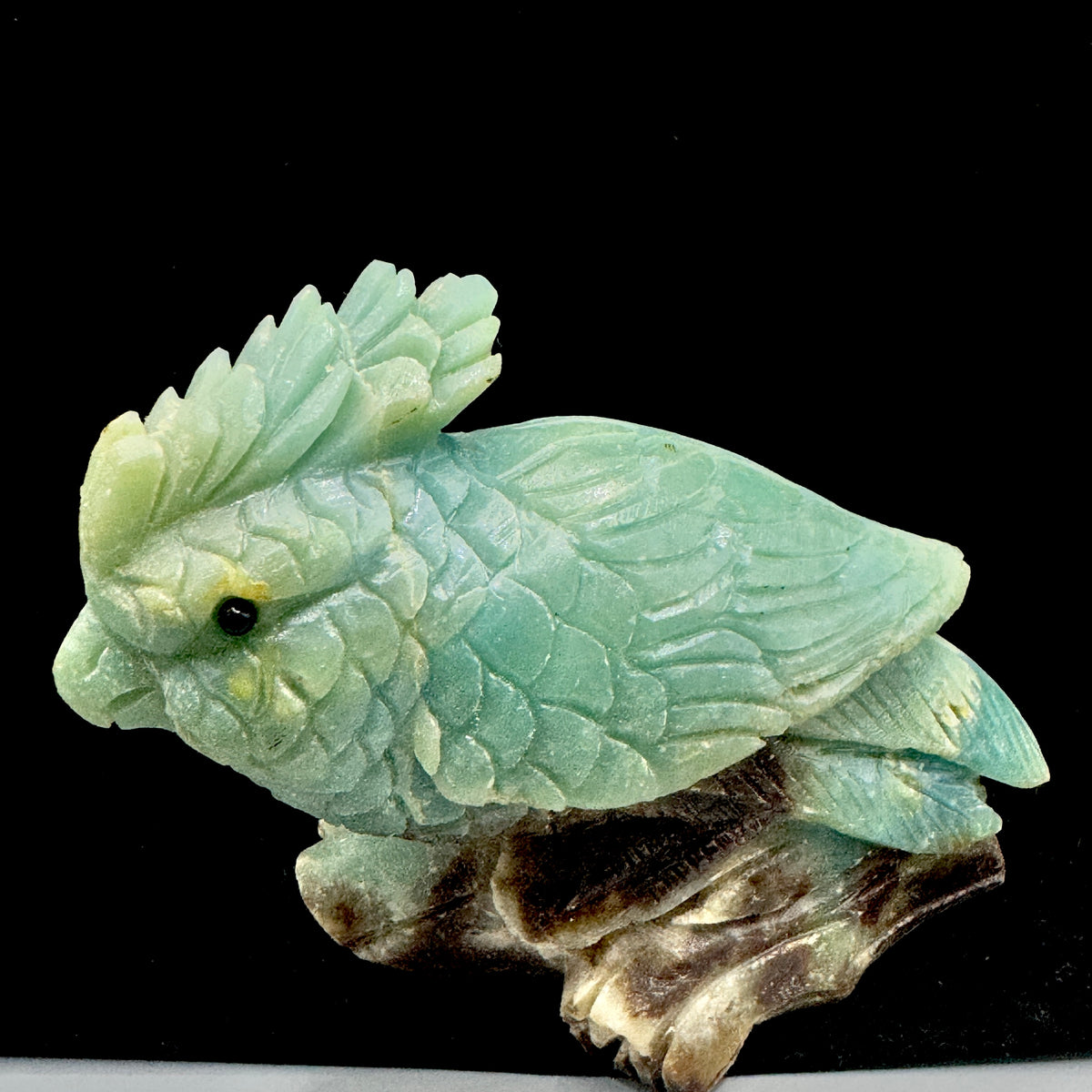 The parrot statue is elegantly positioned on a smooth, natural wooden base, emphasizing its stability and artistic presentation.