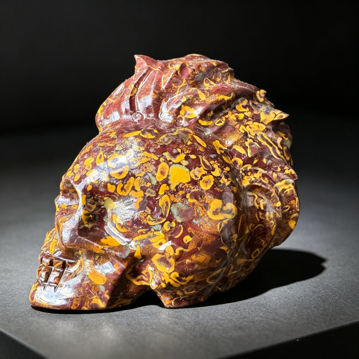 Natural stone carved skull sculpture with red, brown and golden natural patterns, shown from a top back angle.