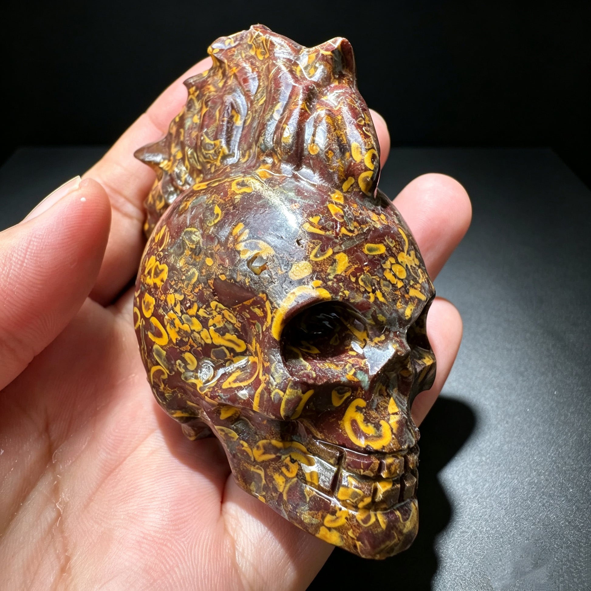 Natural stone carved skull sculpture with red, brown and golden natural patterns.