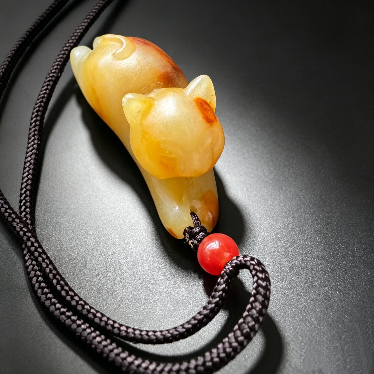 Carved natural jade cat pendant three quarter view with decorative cord