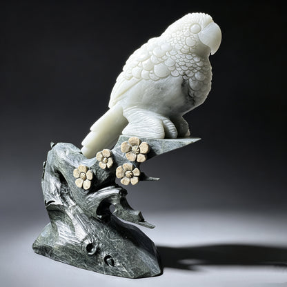 Natural stone hand carved parrot sculpture showing layered wing feathers and long tail from the opposite side.