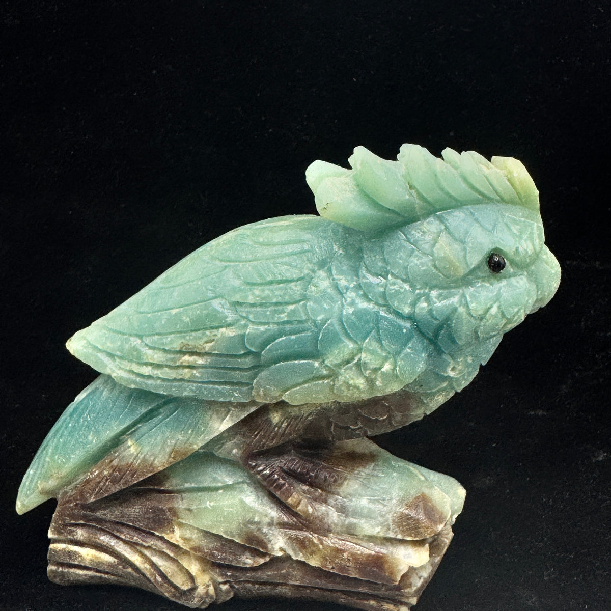 The parrot statue elegantly positioned on a smooth, natural wooden base, emphasizing its stability and beauty.


